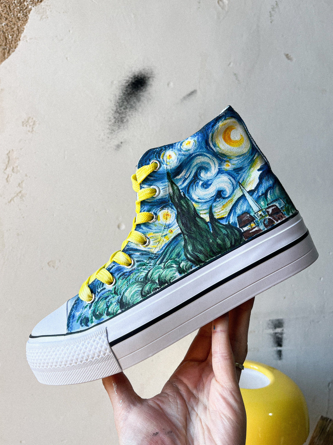 Mano con una zapatilla tipo converse de tela pintada con la noche estrellada de Vincent Van Gogh en azules,verdes y amarillos, con cordones amarillos